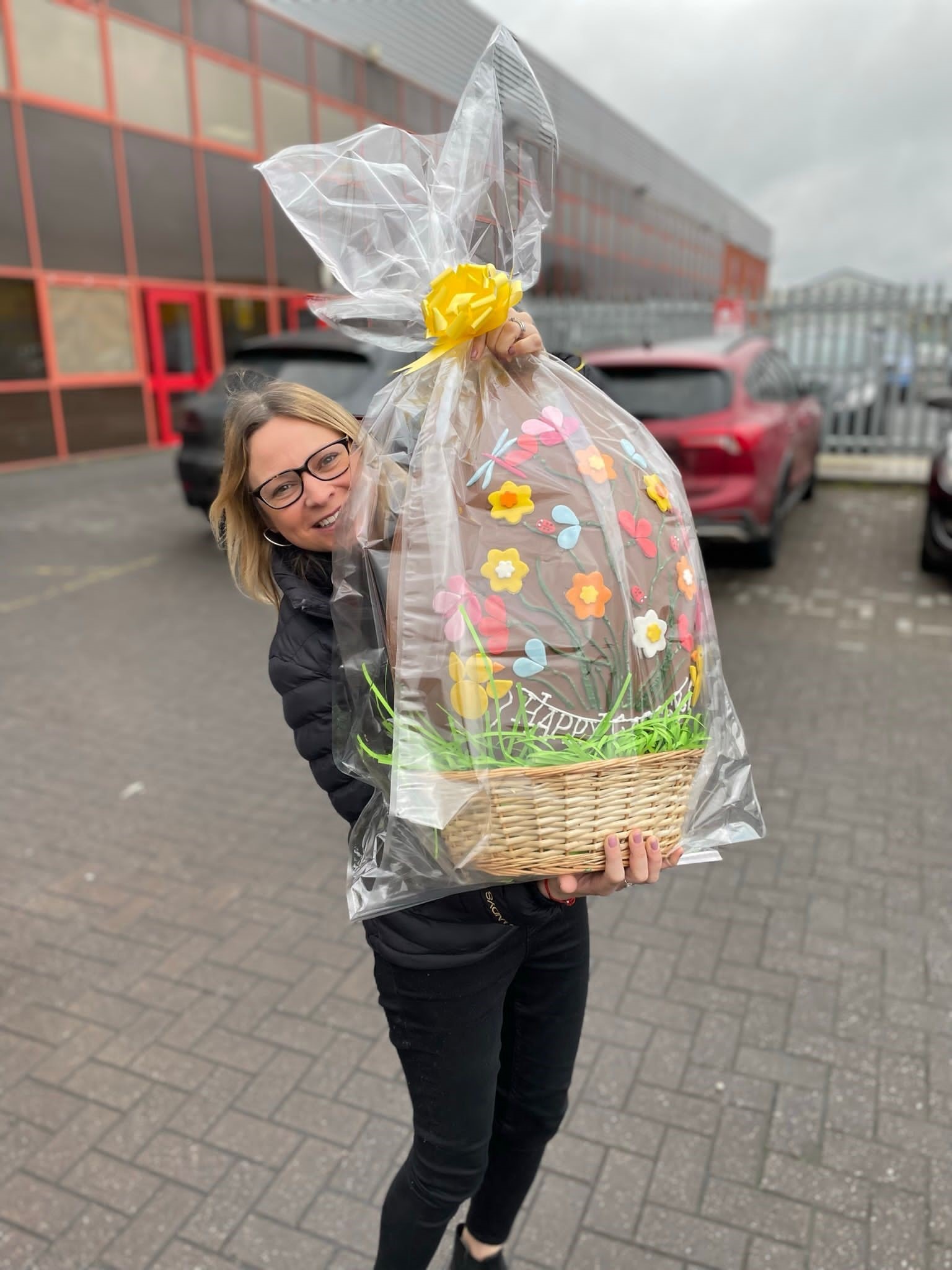 This shows our Fundraising Coordinator Sarah holding a giant chocolate egg. It's in a wicker basket and is wrapped in cellophane.  