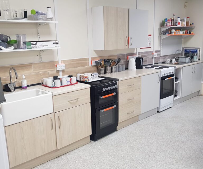 This shows appliances in our sight friendly kitchen. There's cupboards, ovens, a hob and items including kettles and mugs on the work surface.