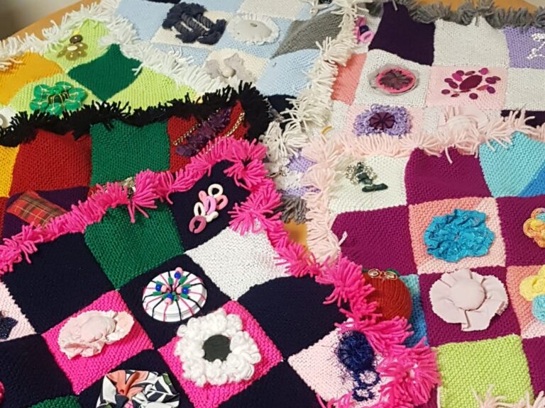 This shows some knitted patchwork blankets made by out members. They are brightly coloured and all decorated with different types of flowers.