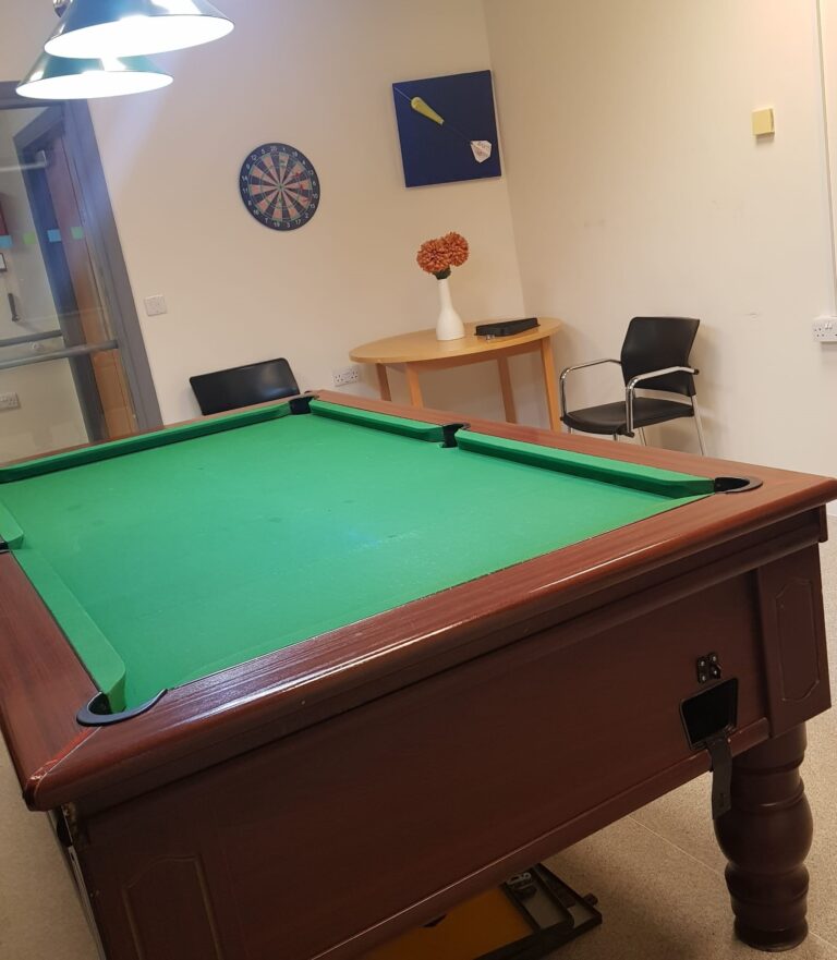 This shows a pool table in our quiet room. In the background there's a darts board and a table with a couple of chairs.