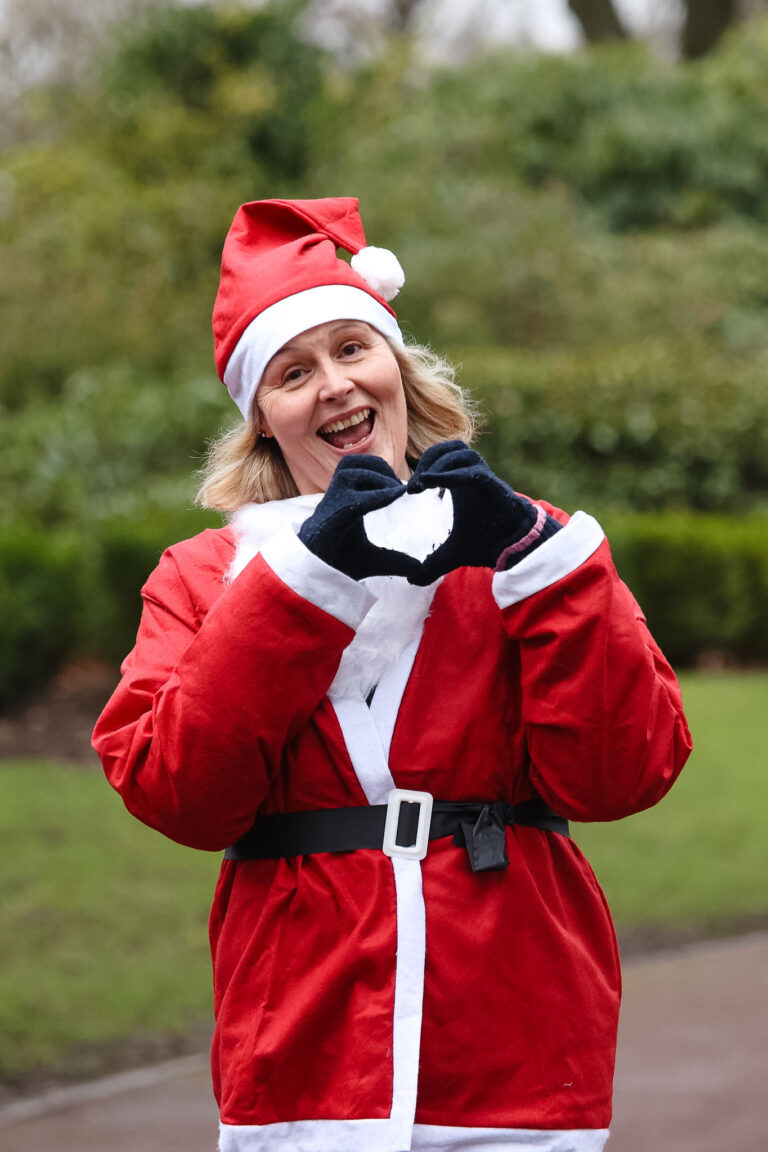 This image shows a female runner, in her Santa outfit making a heart sign with her hands as she runs.